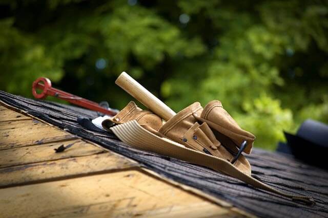 Roofer's troolbelt with assorted tools in it sitting on edge of roof.
